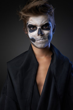 Teen with make-up of skull in black cloak unhappy