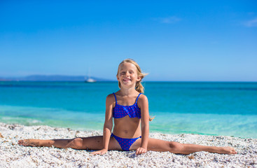 Fototapeta na wymiar Adorable little girl making leg-split on tropical white sandy