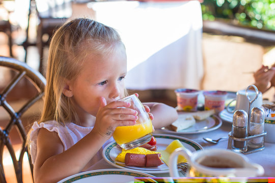 Adorable little girl having breakfast and drinking fruit
