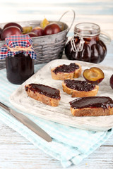 Bread with plum jam and plums on wooden table