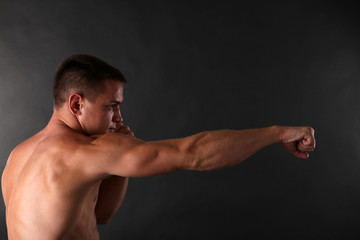 Fototapeta na wymiar Handsome young muscular sportsman boxing on dark background
