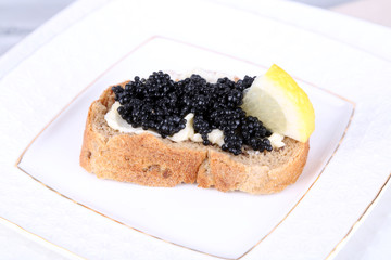 Slice of bread with butter, black caviar and lemon on plate