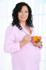 Young pregnant woman holding bowl with salad on light