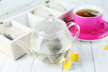 Cup of tea, teapot and tea bags on wooden table close-up