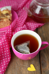 Cup of tea, teapot and tea bags on wooden table close-up