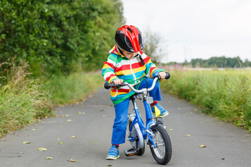 Adorable kid boy in red helmet and colorful raincoat riding his