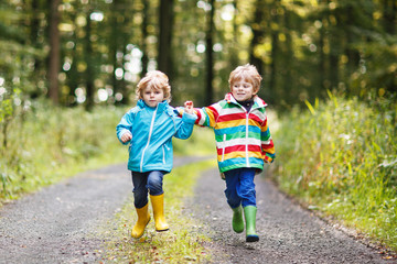 Two little sibling boys in colorful raincoats and boots walking