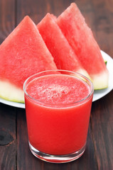 Watermelon cocktail in glass and slices on wooden table