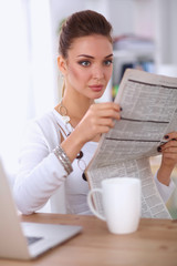 Cute businesswoman holding newspaper sitting at her desk in