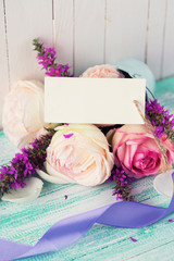 Postcard with fresh flowers and tag on wooden background.