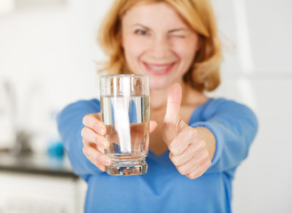 Woman holding a glass of water and showing thumbs up