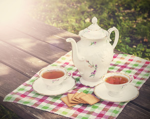 Vintage picture of tea cups and teapot on wooden table in garden.