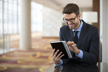 Smiley businessman with glasses using tablet at the hotel lobby
