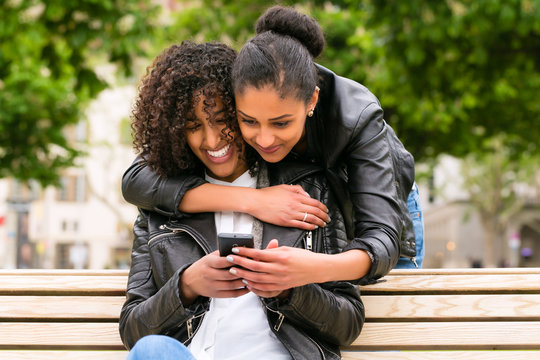 Beste Freunde chatten mit Smartphone auf Parkbank