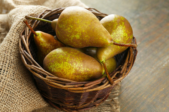 Ripe pears in wicker basket, on wooden background