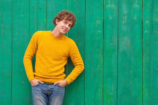 Smiling Curly Man In Yellow Sweater On Green Wooden Background