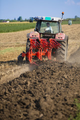 Naklejka premium Farmer plowing stubble field with red tractor