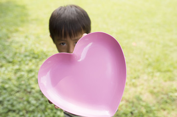 Boy hiding his face with dish heart-shaped