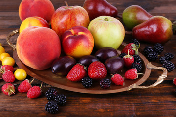 Naklejka na ściany i meble Different berries and fruits on tray on wooden table close-up
