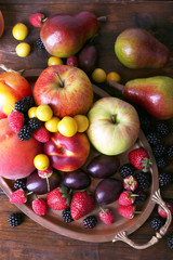 Different berries and fruits on tray on wooden table close-up