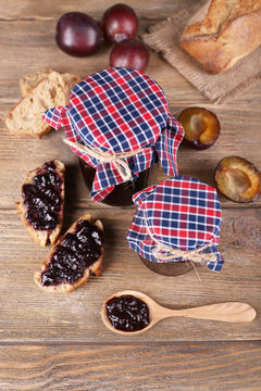 Tasty plum jam in jars and plums on wooden table