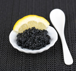 Black caviar with lemon on plate on dark fabric background