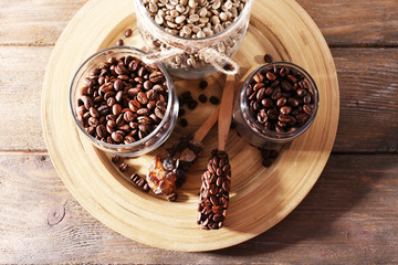 Coffee beans in jars on bamboo plate on wooden background