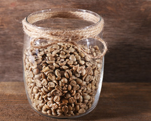 Glass jar of coffee beans  on wooden table on wooden background