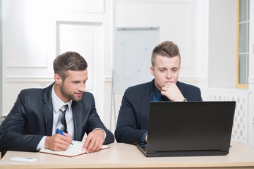 Two handsome businessmen in office working on some project, look