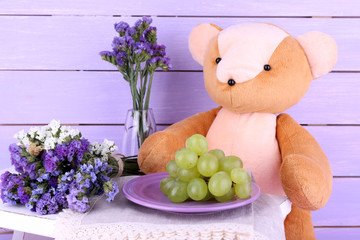Toy bear and grapes on plate on wooden wall background