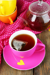 Cup of tea, teapot and tea bags on wooden table close-up