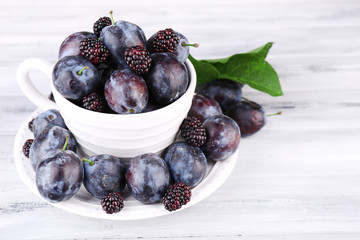 Ripe sweet plums in big cup, on grey wooden table