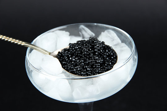 Black caviar in metal spoon and ice in goblet on dark