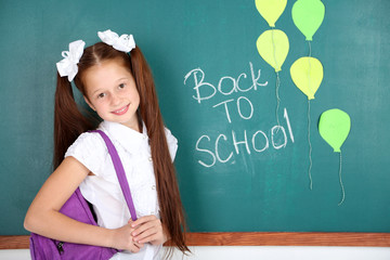 Cute girl standing near blackboard in classroom