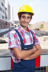 Lächelnder Bauarbeiter mit verschränkten Armen auf Baustelle