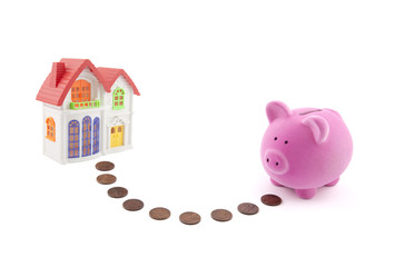 Saving for a house. Piggy bank with coins and house miniature.