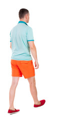 Back view of going  handsome man in shorts.  walking young guy
