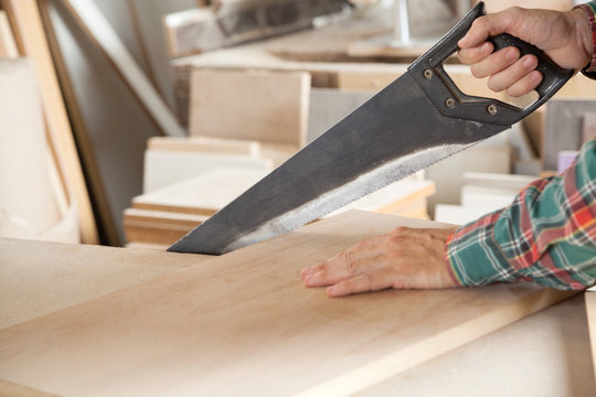 Carpenter Cutting Wooden Plank With Handsaw
