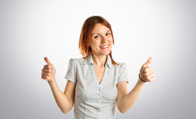 Pretty young girl with thumbs up over grey background