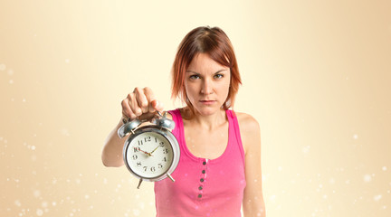 Serious redhead girl holding a clock over ocher background