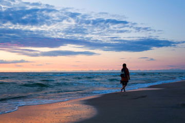 Naklejka premium Sea beach at sunset with water splashes with woman silhouette