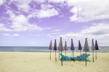 Group of beach chairs and closed umbrellas on white sand beach w