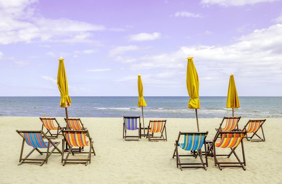 Group of beach chairs and closed umbrellas on white sand beach w - Powered by Adobe