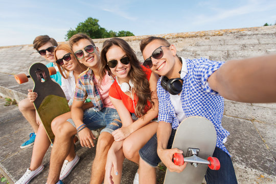 group of smiling friends with smartphone outdoors