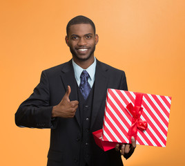 Smiling business man holding present giving thumb up
