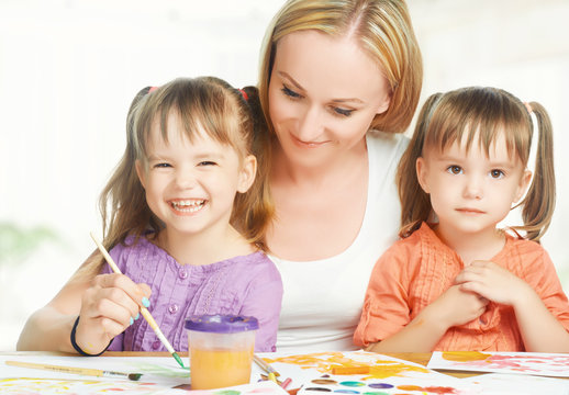 children twin sisters draw paints with her mother