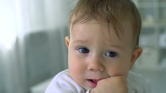 Close up of lovely Caucasian baby boy rubbing his gums while having teething pain, childhood and parenting concepts