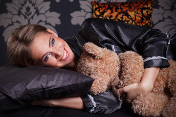 Beautiful young woman hugging a teddy bear in the bed