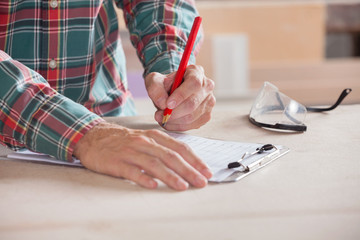 Obraz premium Carpenter Writing Notes On Clipboard At Table