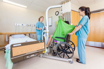 Female Nurses Transferring Patient From Hydraulic Lift To Wheelc - Powered by Adobe